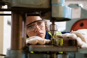 Close-up of female apprentice using yoke machine. Female engineer is wearing protective glasses in factory. She is working in manufacturing industry.