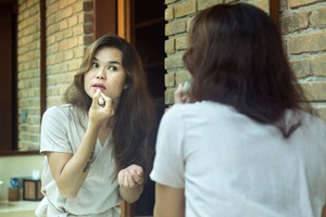 In a luxurious bathroom environment, a masculine mid-age transgender of Asian origin is preparing herself by making up in front of a very large mirror. digital safety sexting safe sex contraceptives coronavirus